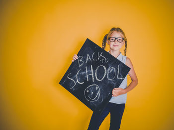 Portrait of smiling young woman standing against yellow wall