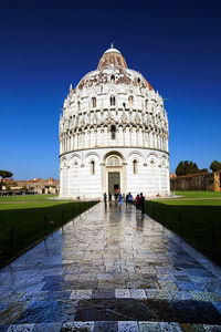 Pathway amidst grassy field leading towards pisa baptistery against clear blue sky