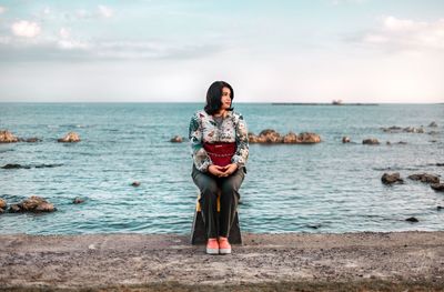 Woman sitting at beach against sky