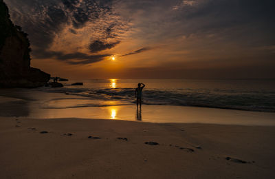 Silhouette man standing on beach against sky during sunset