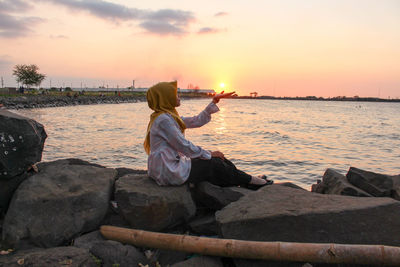 Rear view of woman looking at sea against sky during sunset