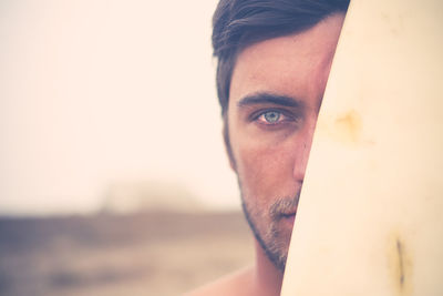 Portrait of young surfer hiding behind surfboard, close-up