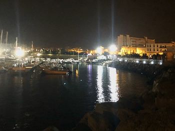 Illuminated buildings by river against sky at night