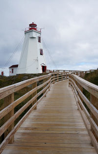 Pier leading towards lighthouse against sky