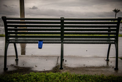 Empty bench by railing against sky