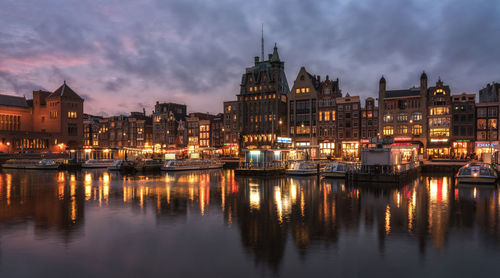 River by illuminated city against sky at dusk