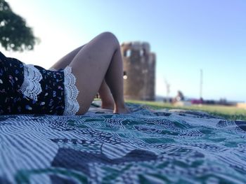 Low section of woman on retaining wall against clear blue sky