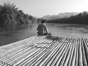 Man sitting on lake against clear sky