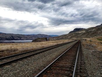 Railroad track leading towards mountain against sky