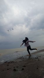 Rear view of woman flying over beach against sky