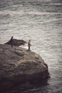 People fishing on rock by sea