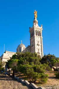 Low angle view of trees and building against blue sky