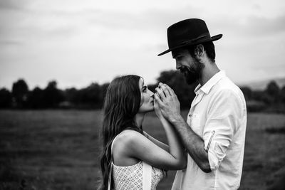 Side view of romantic couple holding hands while standing on field against sky