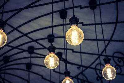 Low angle view of illuminated light bulbs hanging against sky
