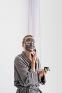 Womens health. spa and wellness. woman in gray bathrobes applying face mask in the bathroom looking