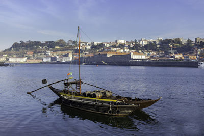 Sailboats moored on sea by buildings against sky in city