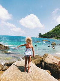 Full length of boy on rock at beach against sky