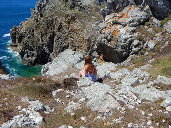 Rear view of woman sitting on cliff by sea