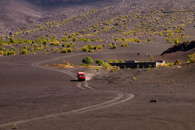 A red minibus drives along a dust road of lava ash on a vulcano flank of pico do fogo, cape verde