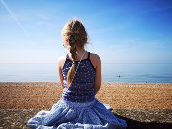 Woman sitting on shore at beach against sky