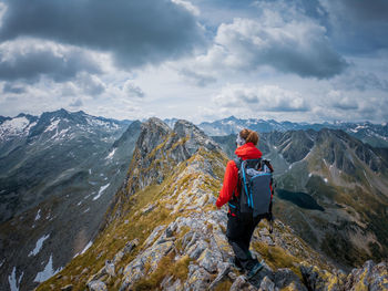 Rear view of woman hiking on rocky mountain peak against sky