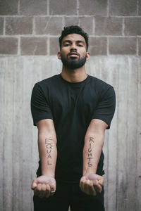 Portrait of male activist showing equal rights written on hand against wall