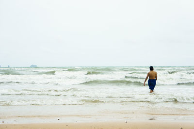 Rear view of man walking on beach against clear sky