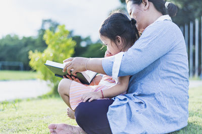 Side view of woman using digital tablet while sitting on field