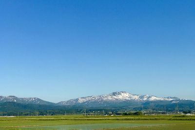 Scenic view of field and mountains against clear blue sky