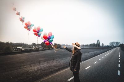 Woman with balloons standing on street against clear sky