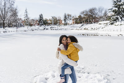 Smiling mother carrying daughter while standing on land during winter