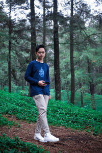 Full length portrait of young man standing at forest