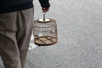 Midsection of person carrying bird cage on footpath