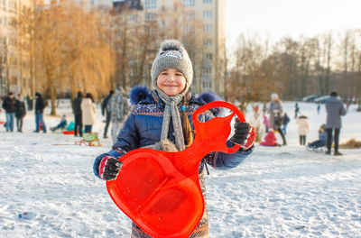 Portrait of smiling girl holding sled on snow covered field