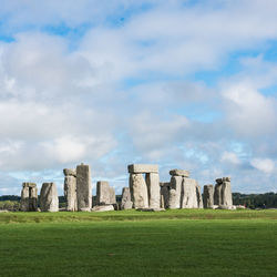 Megalith rocks on grassy field against cloudy sky