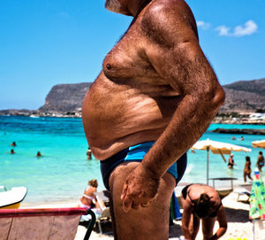 Rear view of shirtless man standing at beach against sky
