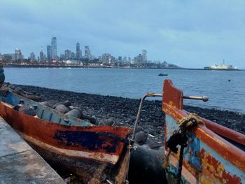 Rusty ship in sea against sky in city