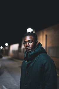 Portrait of man standing against illuminated wall at night