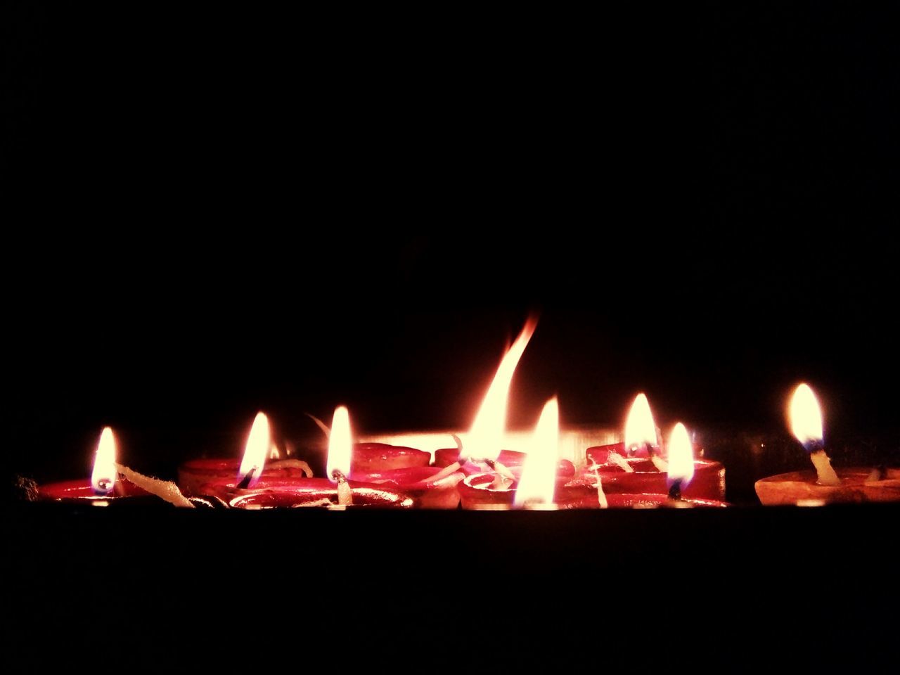 CLOSE-UP OF BURNING CANDLES IN DARKROOM