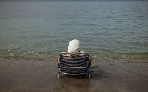 Rear view of adult man siting on chair on beach