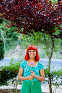 Portrait of smiling woman holding flower standing against plants