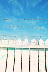 Wooden fence and barbed wire against blue sky