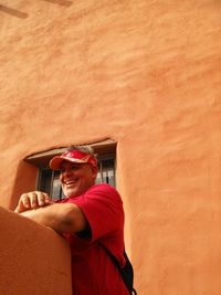 Low angle view of smiling man standing against orange wall