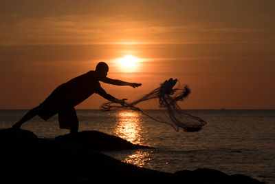 Silhouette man standing by sea against orange sky