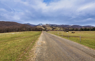 Empty road amidst field against sky