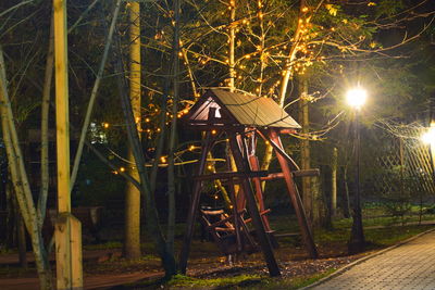 Illuminated street light by trees at night