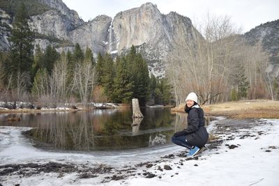 Woman sitting on snow covered landscape against lake