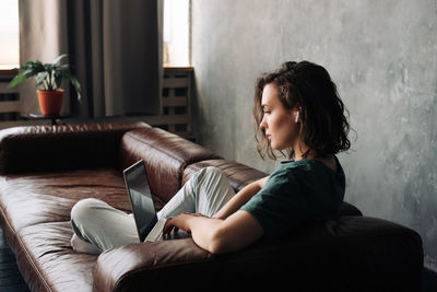 Side view of young woman sitting on sofa at home