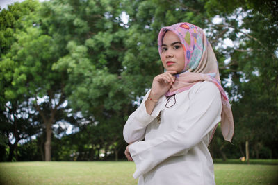 Young woman in hijab standing against trees