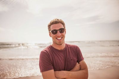 Portrait of young man wearing sunglasses at beach against sky